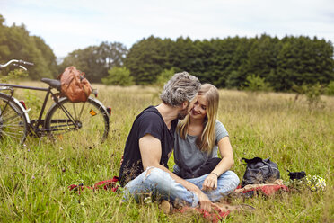 Romantisches Paar sitzt auf einer Picknickdecke in einem ländlichen Feld - CUF16274