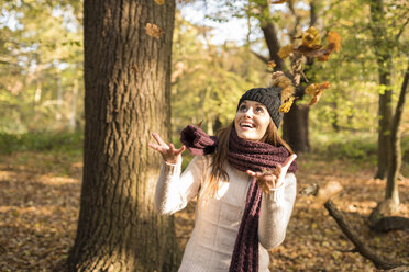 Junge Frau im Wald, die Herbstblätter in die Luft wirft - CUF16306