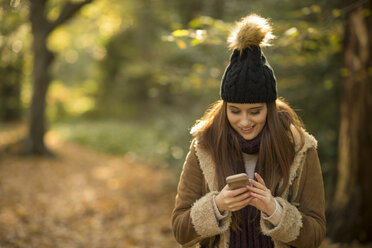 Junge Frau im Wald, schaut auf ihr Smartphone, lächelt - CUF16326