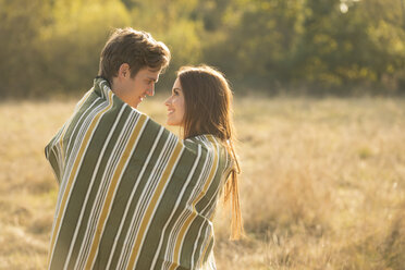 Junges Paar in ländlicher Umgebung, in eine Decke gewickelt, von Angesicht zu Angesicht, lächelnd - CUF16328