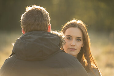 Junges Paar auf einem Feld, junge Frau schaut dem Mann über die Schulter - CUF16331