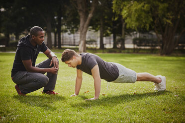 Personal Trainer instruiert jungen Mann bei Liegestützen im Park - CUF16385