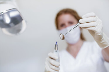 Low angle view of dentist wearing mask and protective gloves holding dental equipment and dental mirror - CUF16408