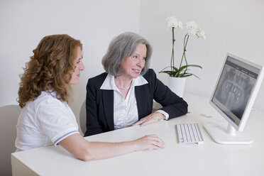 Senior woman and mature woman at desk discussing x-ray image on computer screen smiling - CUF16411