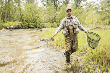 Mann im Fluss mit Wathose und Fischernetz schaut lächelnd in die Kamera - CUF16443