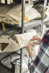 Hand of scientist pointing at seed envelope in plant growth research centre warehouse - CUF16453