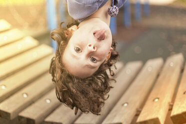 Girl in playground hanging upside down looking at camera sticking out tongue - CUF16573