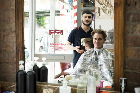 Spiegelbild eines Friseurs mit Spiegel, der einem lächelnden Kunden einen Haarschnitt zeigt - CUF16740