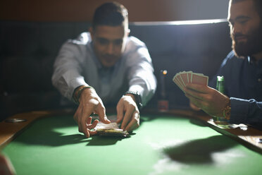 Man picking up card game winnings at pub card table - CUF16770