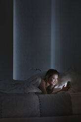 Young woman lying in bed reading smartphone texts at night - CUF16826