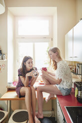 Zwei junge Frauen sitzen am Küchentisch und unterhalten sich - CUF16829