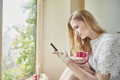 Junge Frau liest Smartphone-Text in der Küche, lizenzfreies Stockfoto