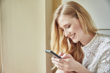 Young woman reading smartphone text at home - CUF16833