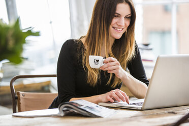 Young woman in city apartment drinking espresso whilst typing on laptop - CUF16843