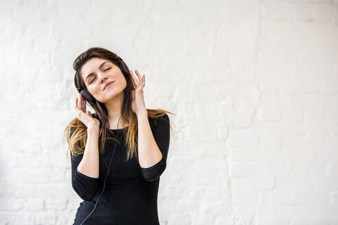 Schöne junge Frau, die sich zu Kopfhörermusik vor einer weißen Wand wiegt - CUF16852
