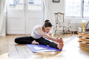 Junge Frau übt Yoga, berührt ihre Zehen in der Wohnung - CUF16863