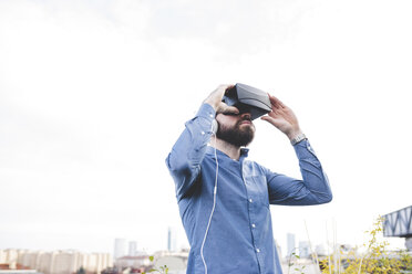 Junger männlicher Designer testet Virtual-Reality-Headset auf der Dachterrasse seines Büros - CUF16904