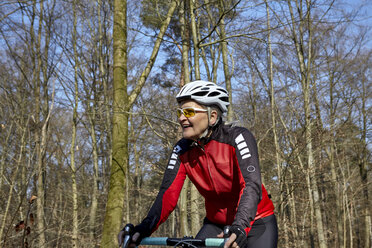 Woman wearing cycling helmet and sunglasses cycling, looking away smiling - CUF17049