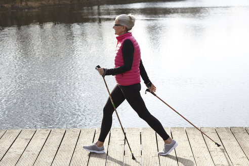 Ganzkörperansicht einer Frau beim Nordic Walking am Teich - CUF17052