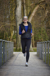 Frontalansicht einer Frau auf einem Holzweg beim Joggen, die lächelnd in die Kamera schaut - CUF17064