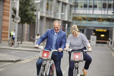 Mature dating couple laughing whilst cycling on hire bicycles, London, UK stock photo