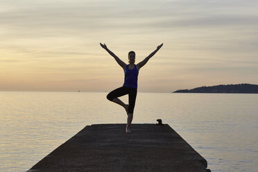 Junge Frau auf dem Pier stehend, in Yoga-Position, bei Sonnenuntergang - CUF17122