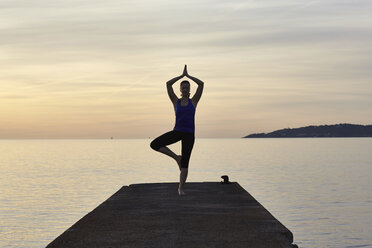 Junge Frau auf dem Pier stehend, in Yoga-Position, bei Sonnenuntergang - CUF17123