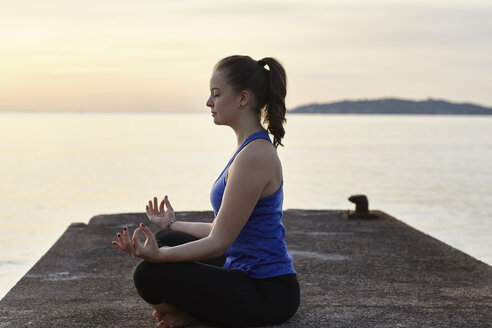 Junge Frau, die bei Sonnenuntergang auf dem Pier sitzt, in Yoga-Position - CUF17125