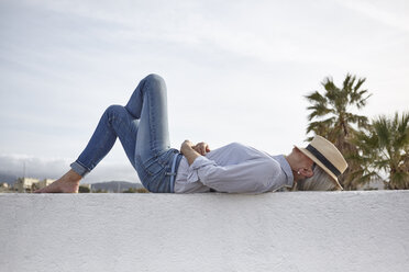 Mature woman lying on wall, hat covering face - CUF17129