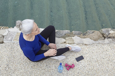 Ältere Frau sitzt im Freien, Handgewichte, Wasser und Smartphone neben sich, Blick von oben - CUF17134