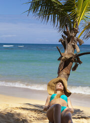 Junge Frau im Bikini beim Sonnenbaden auf einer Palme am Strand, Dominikanische Republik, Karibik - CUF17209