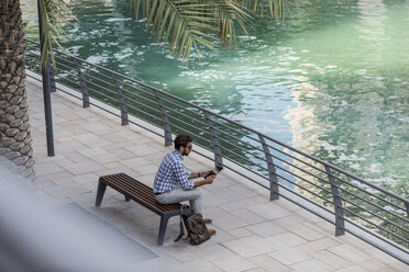 Blick von oben auf einen jungen Mann, der am Wasser sitzt und ein digitales Tablet benutzt, Dubai, Vereinigte Arabische Emirate - CUF17213