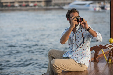 Junger Mann beim Fotografieren vom Boot aus im Jachthafen von Dubai, Vereinigte Arabische Emirate - CUF17241