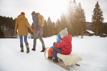 Rückansicht von Eltern, die ihre Söhne auf einem Schlitten durch eine Schneelandschaft ziehen, Elmau, Bayern, Deutschland - CUF17251