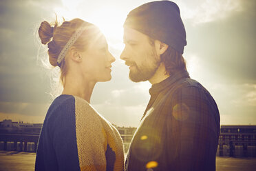 Sunlit portrait of mid adult couple face to face on rooftop parking lot - CUF17267