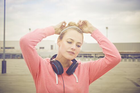Mittlere erwachsene Frau mit Kopfhörern, die ihre Haare auf einem Parkplatz auf dem Dach zusammenbindet - CUF17275