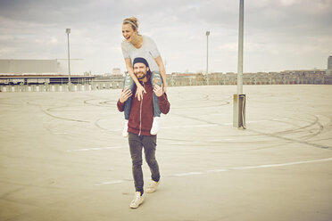 Mid adult man giving shoulder ride to girlfriend on rooftop parking lot - CUF17278
