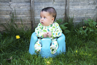 Porträt eines niedlichen Babyjungen, der im Garten auf einem Babytragesitz sitzt - CUF17284