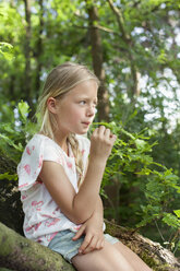 Girl sitting on branch chewing grass - CUF17298