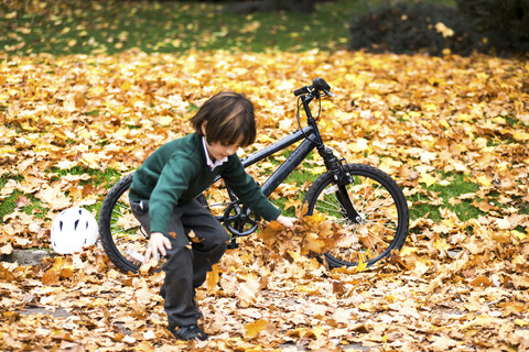 Junge im Park mit Fahrrad spielt im Herbst Blätter, lizenzfreies Stockfoto