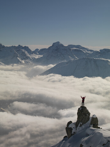 Feiernder Bergsteiger auf dem aus dem Nebel auftauchenden Gipfel, Bettmeralp, Wallis, Schweiz, lizenzfreies Stockfoto