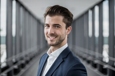 Portrait of smiling young businessman in a passageway - DIGF04501