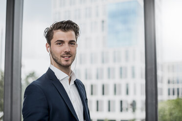 Portrait of confident young businessman wearigng earbuds at the window - DIGF04511