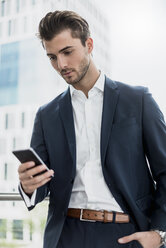 Businessman at the window using cell phone - DIGF04515