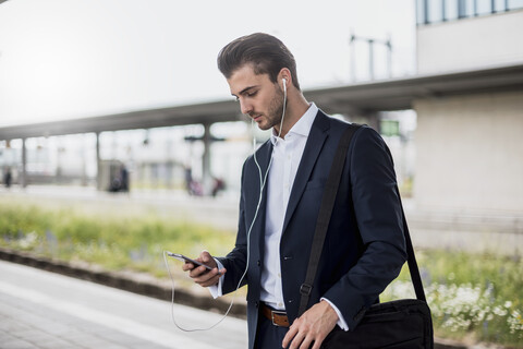 Businessman at the station with earbuds and cell phone stock photo