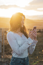 Island, Frau benutzt Smartphone bei Sonnenuntergang - KKAF01089