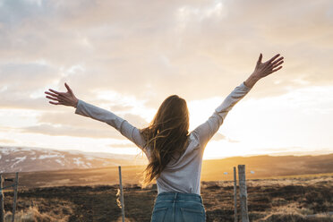 Iceland, young woman with raised arms at sunset - KKAF01090