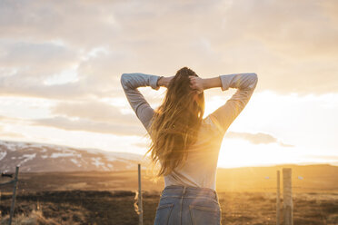 Island, junge Frau mit Händen im Haar bei Sonnenuntergang - KKAF01091