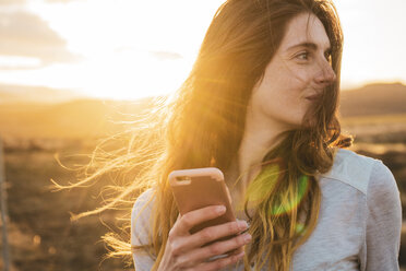 Island, Frau benutzt Smartphone bei Sonnenuntergang - KKAF01093