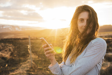 Island, Frau benutzt Smartphone bei Sonnenuntergang - KKAF01094